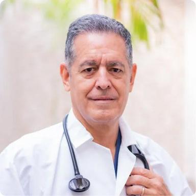 Portrait of a male healthcare provider with gray hair and a stethoscope around his neck, standing confidently in a white coat.